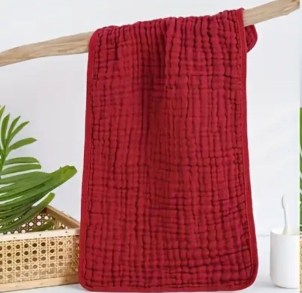 Burgundy textured blanket draped over a wooden rod with plants in the background