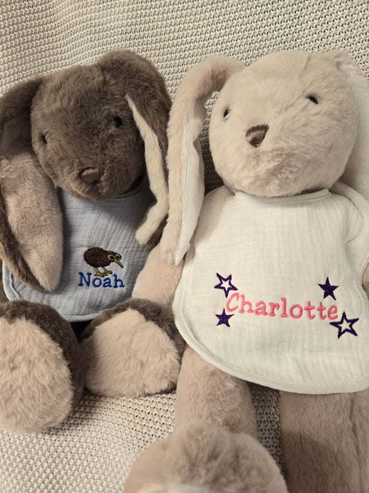 Two plush toys, one brown and one beige, wearing embroidered bibs with names 'Noah' and 'Charlotte'.
