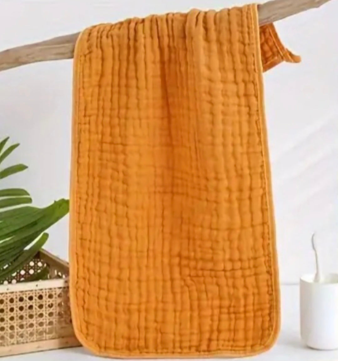 Orange textured fabric hanging on a wooden rod with a plant and candle in the background.