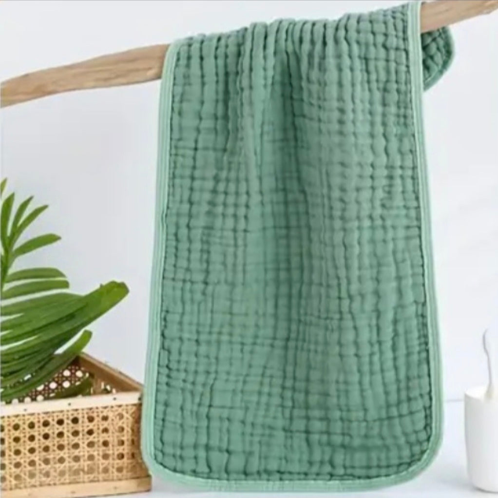 Green textured towel hanging on a wooden rod with a plant and basket in the background.